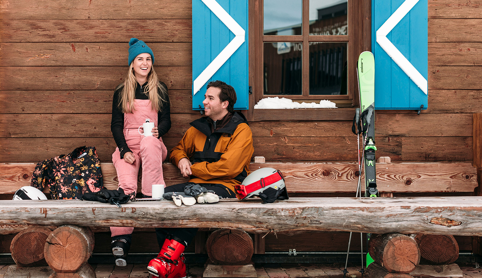 Een man en vrouw zitten met skigear om zich heen voor een berghut