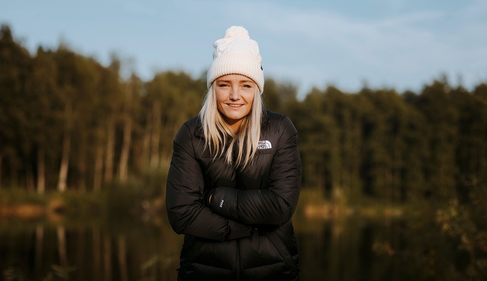 Een jonge vrouw in een dikke jas en een muts lacht in de camera