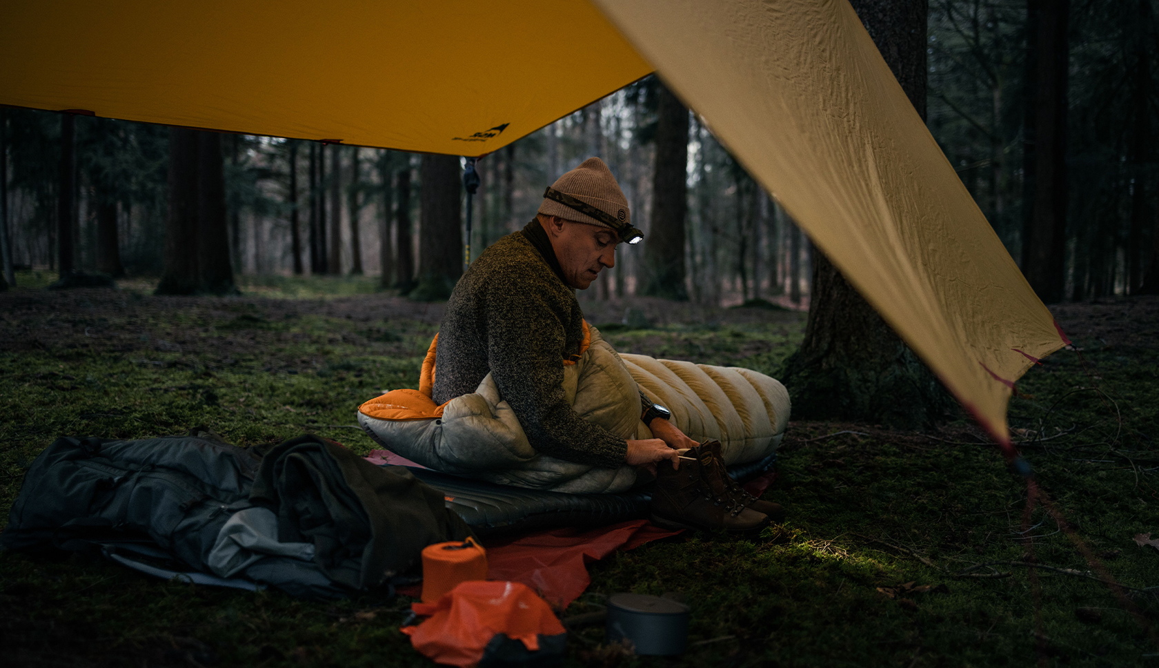 bushcrafter in slaapzak onder tarp