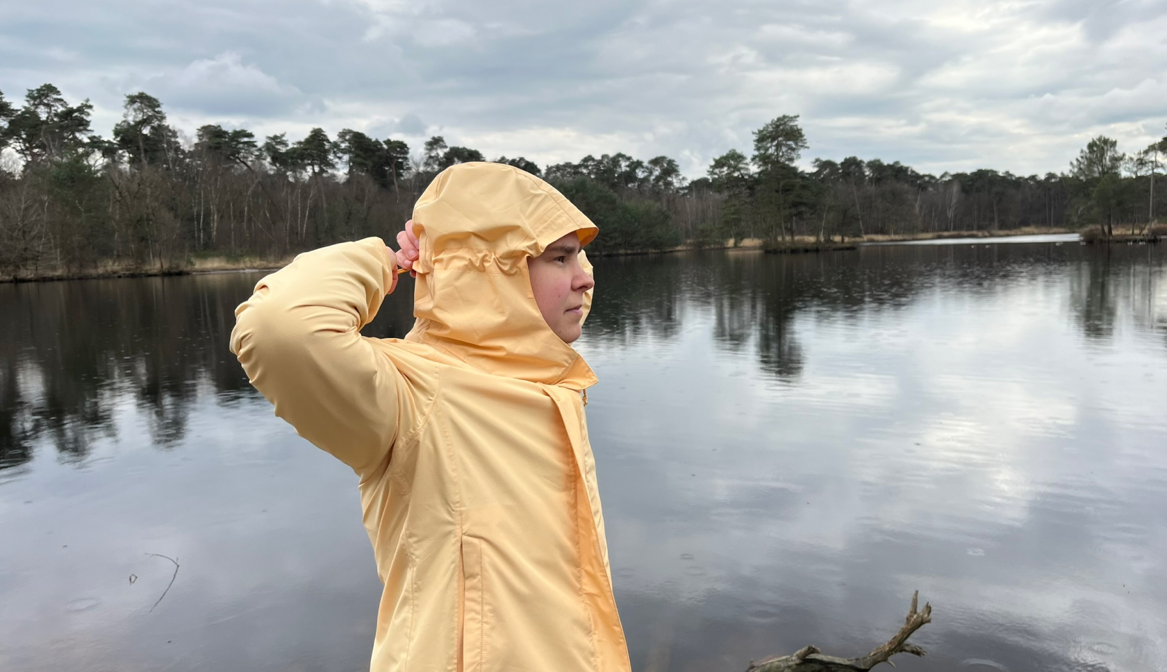 Een vrouw staat voor een meer in het bos