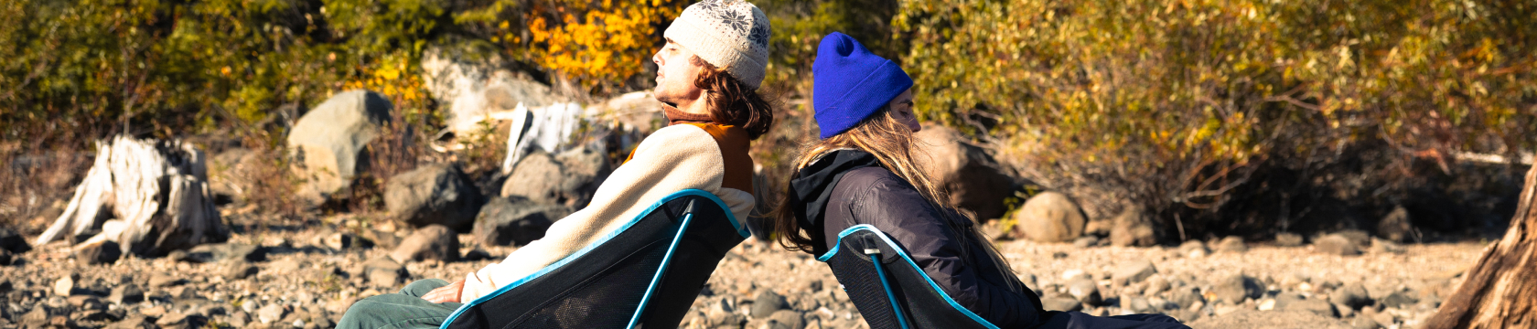 Twee personen zitten op campingstoelen op rotsige grond.