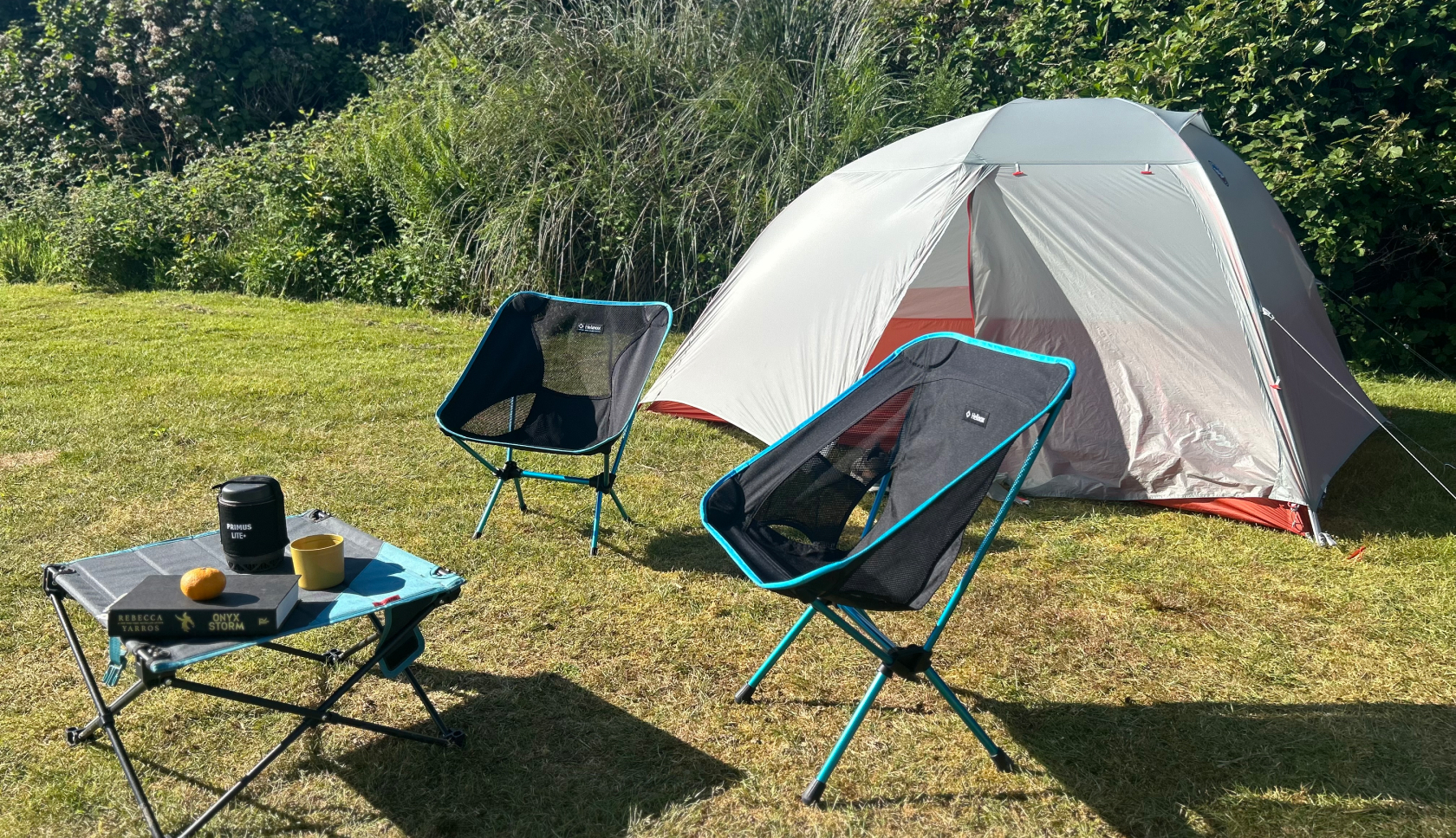 Twee campingstoelen en een campingtafel staan in het gras voor een tent.