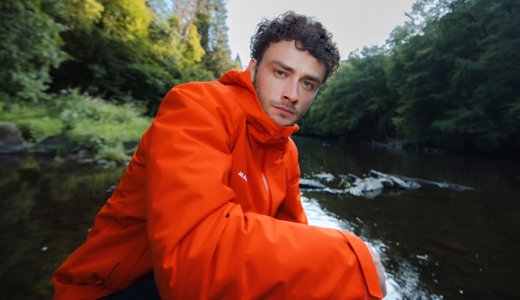 man in rode jas hurkt bij rivier in bos