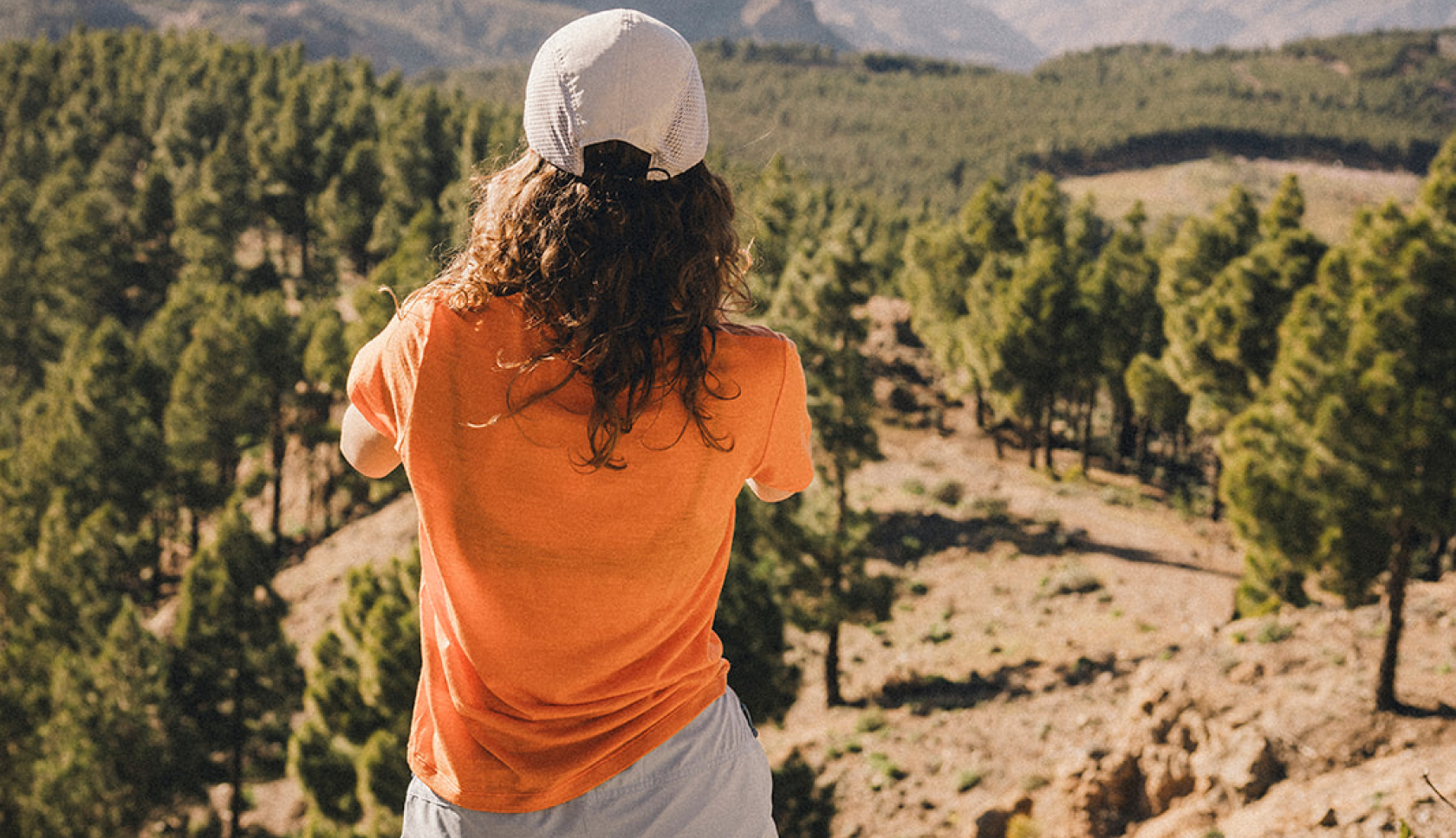 Een vrouw in een oranje Ayacucho-merinoshirt staat met haar rug naar de camera op een heuvel