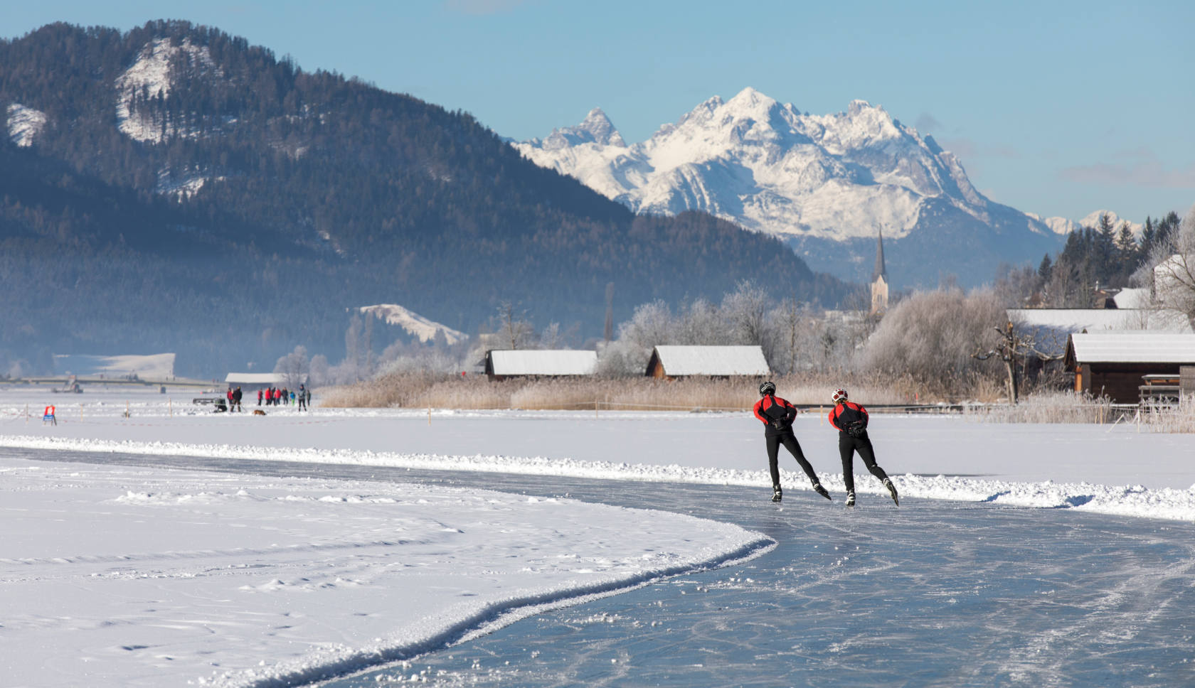professionele schaatsers schaatsen over natuurijs met bergen in de achtergrond