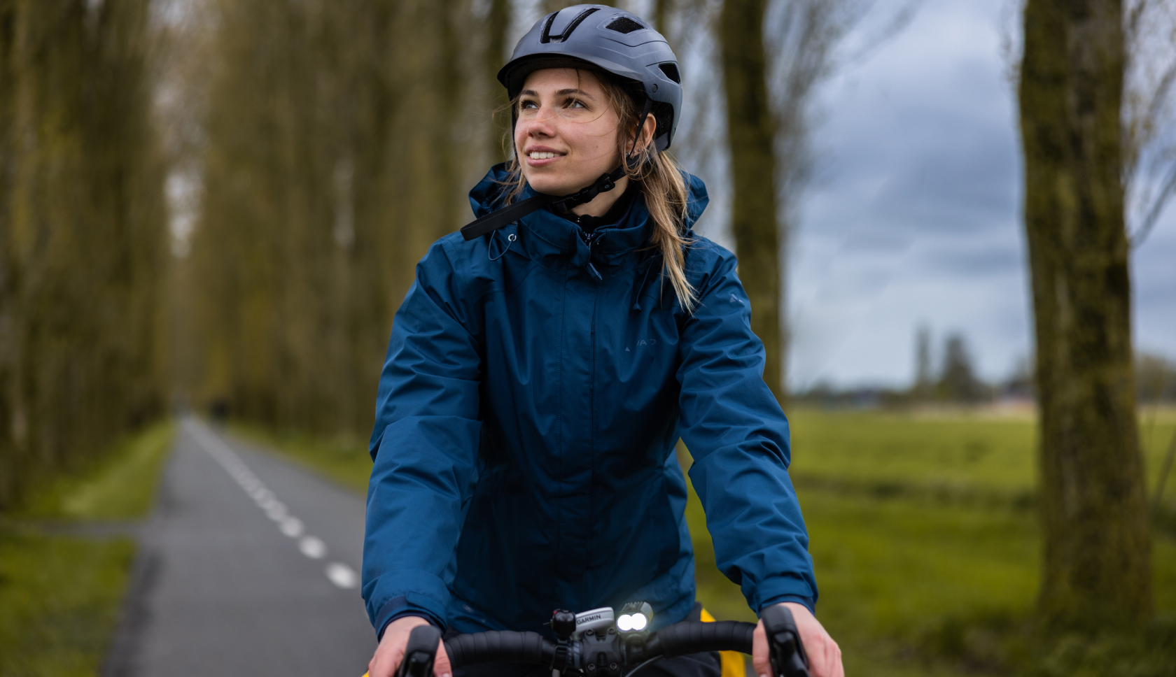 Een jonge vrouw fietst op een verharde weg met zijlangs een rij bomen