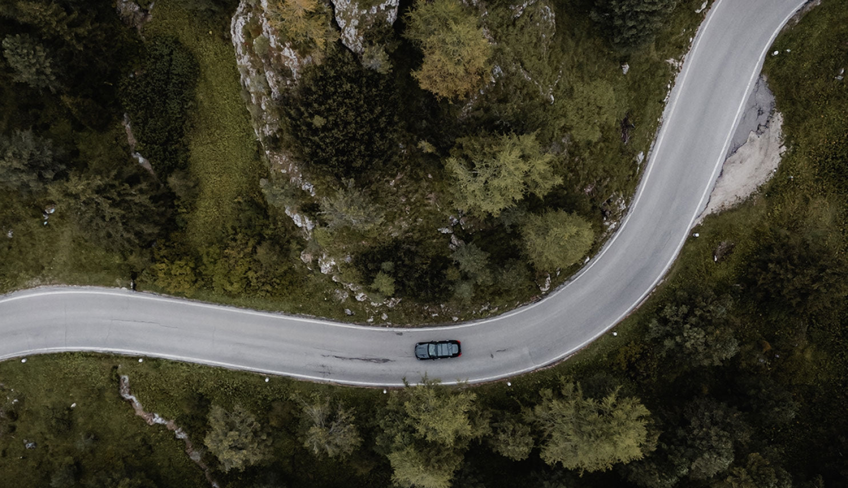 Een auto rijdt op een verharde weg, omgeven door groen
