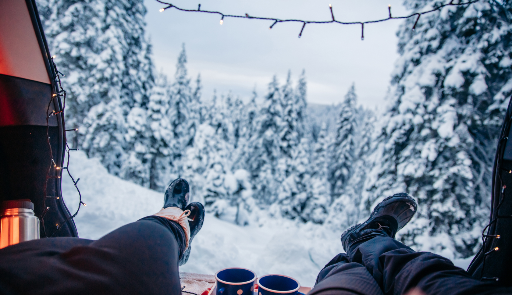 twee personen liggen in de achterbak van een auto met hun voeten richting de sneeuw