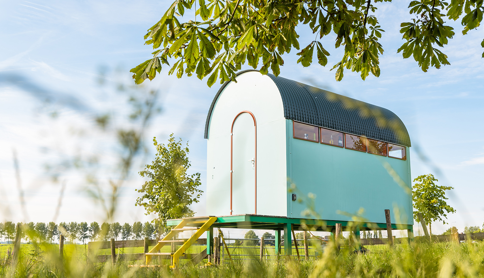 Een houten kleurrijke kampeerhut staat in het weiland.