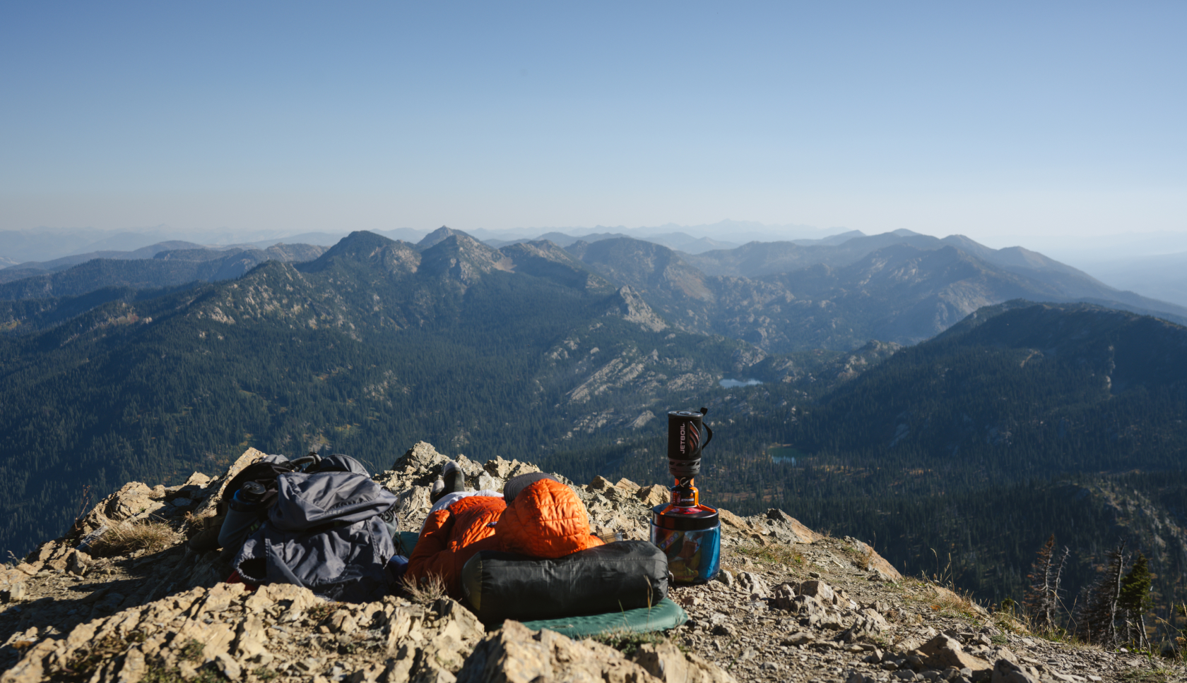 Een persoon ligt op een slaapzak op de grond en kijkt uit over talloze bergtoppen