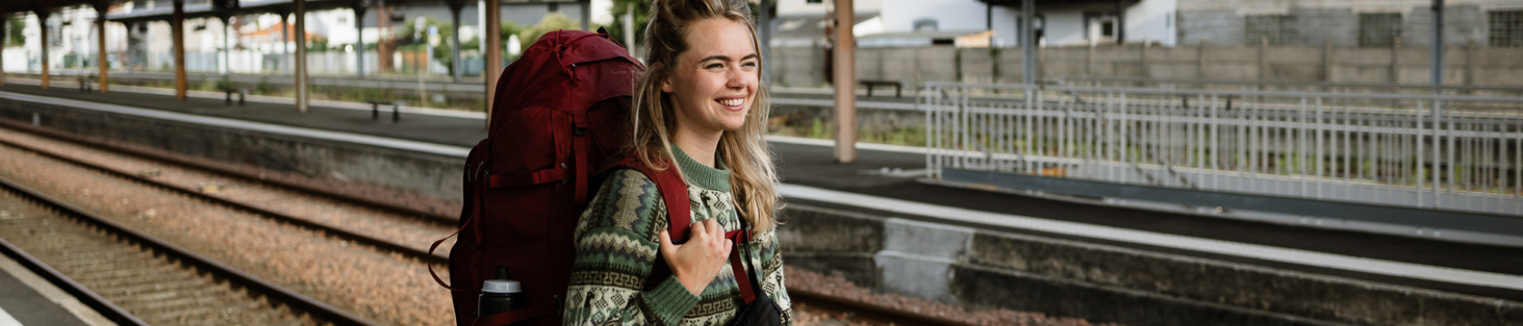 Een jonge vrouw staat op het station met een rode backpack op haar rug