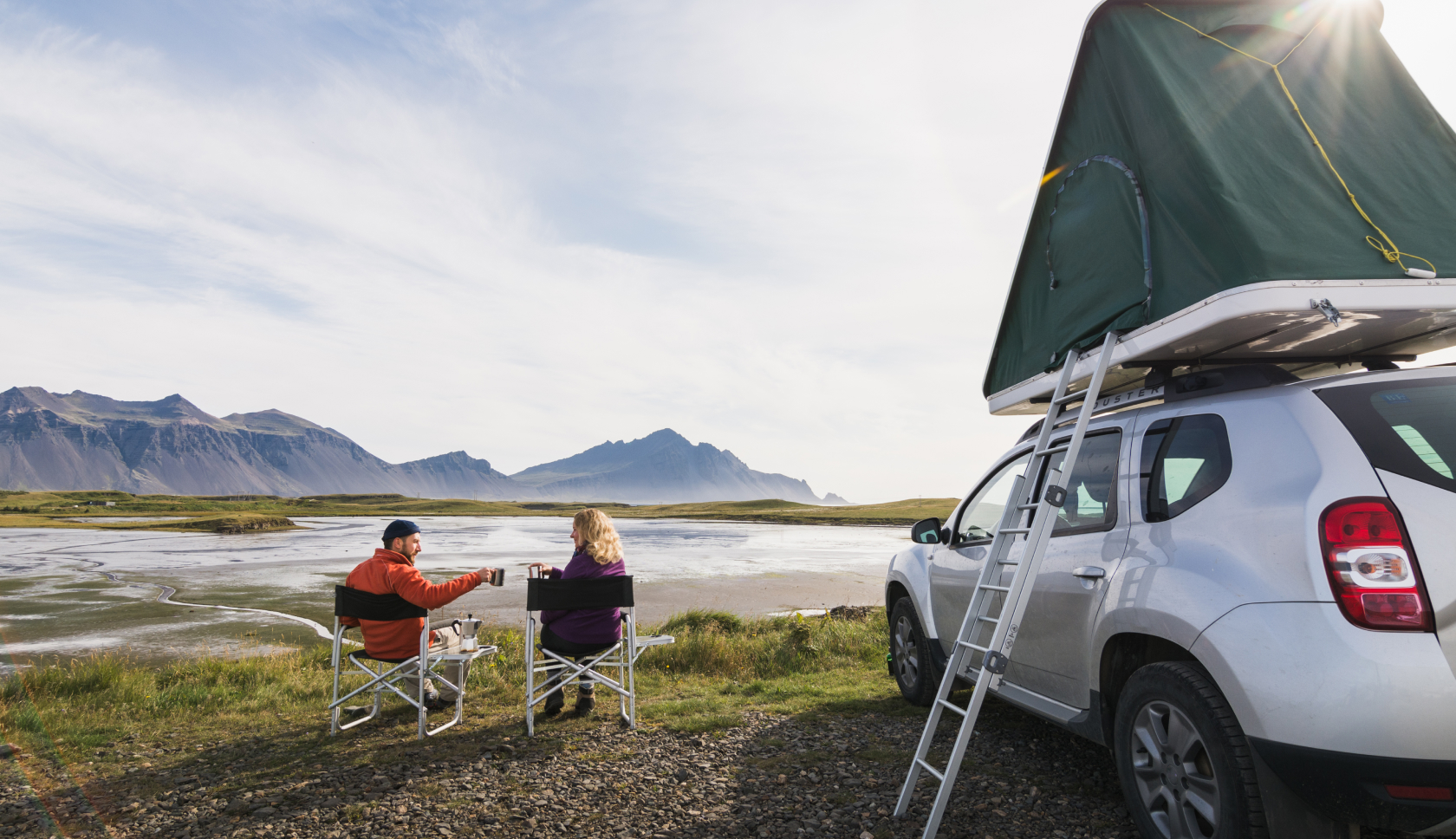 Een stel zit naast een auto met daktent en geniet van het uitzicht op fjorden