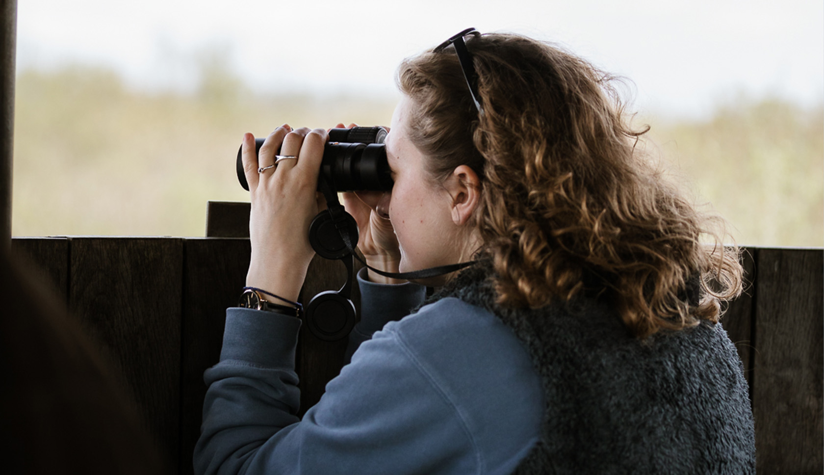 vrouw kijkt naar vogels met verrekijker in vogelhut