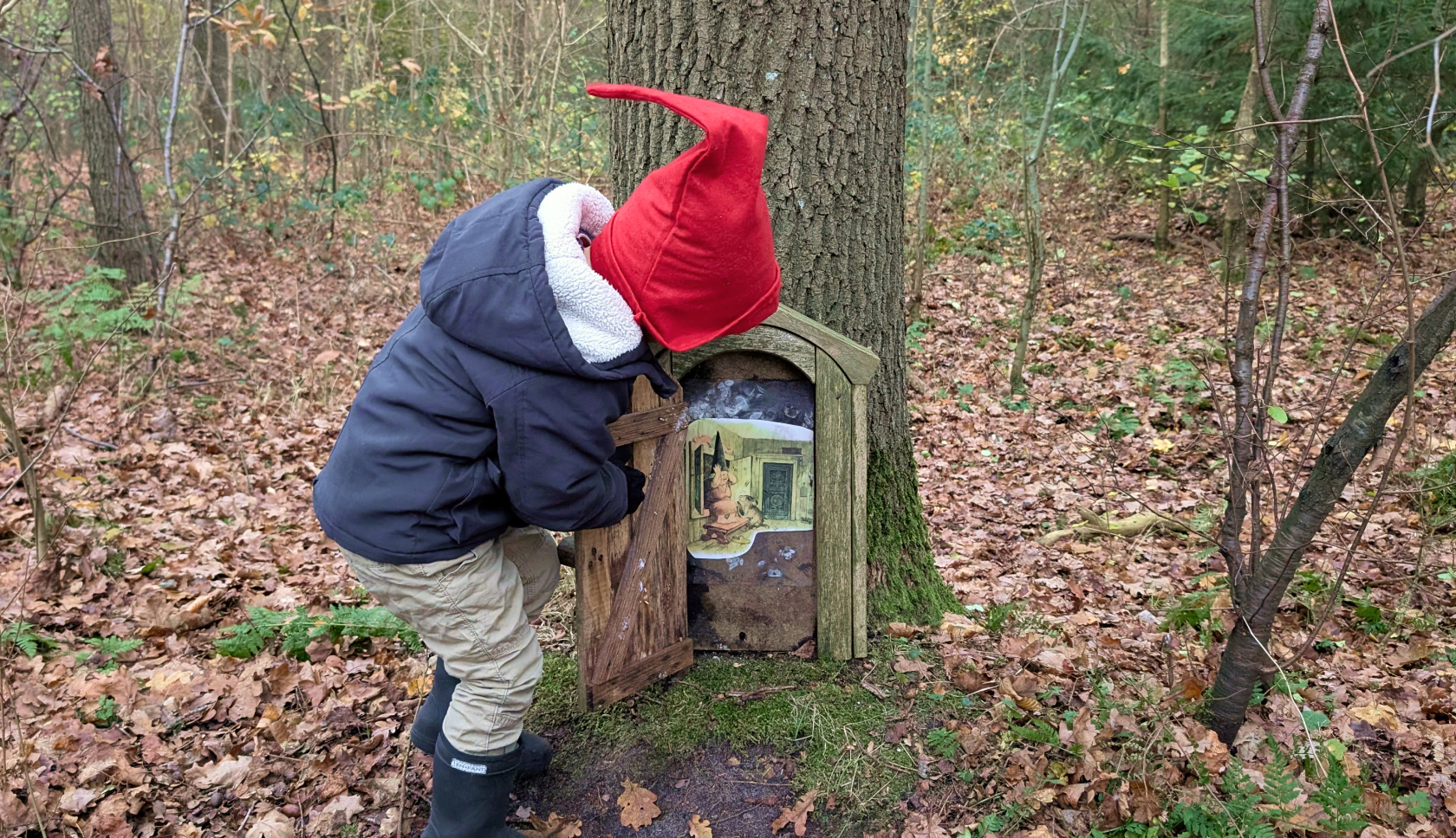 Een kindje met kaboutermuts opent een geheime deur in een boom
