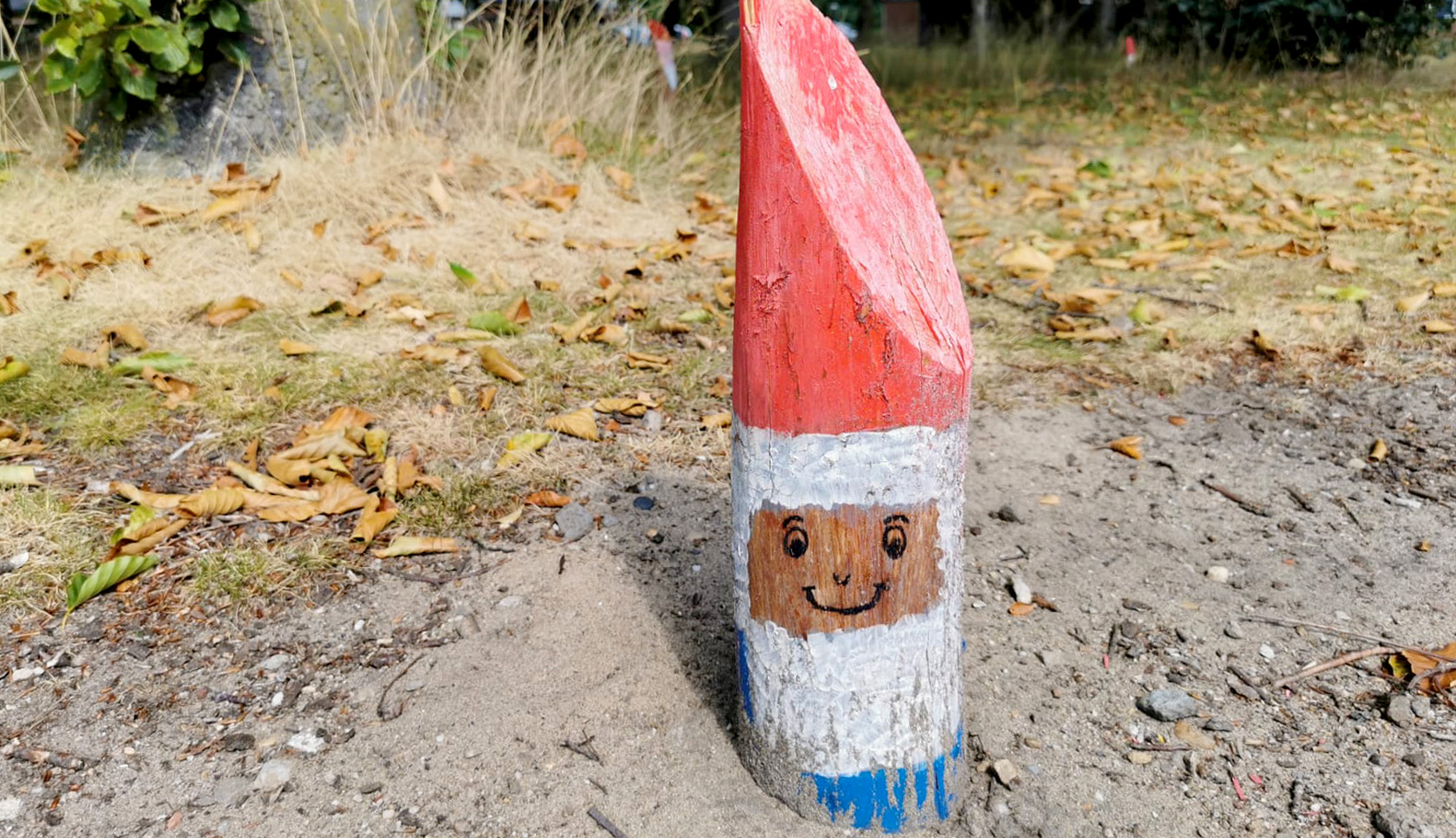 Een klein paaltje in een bos met een beschildering van een kabouter