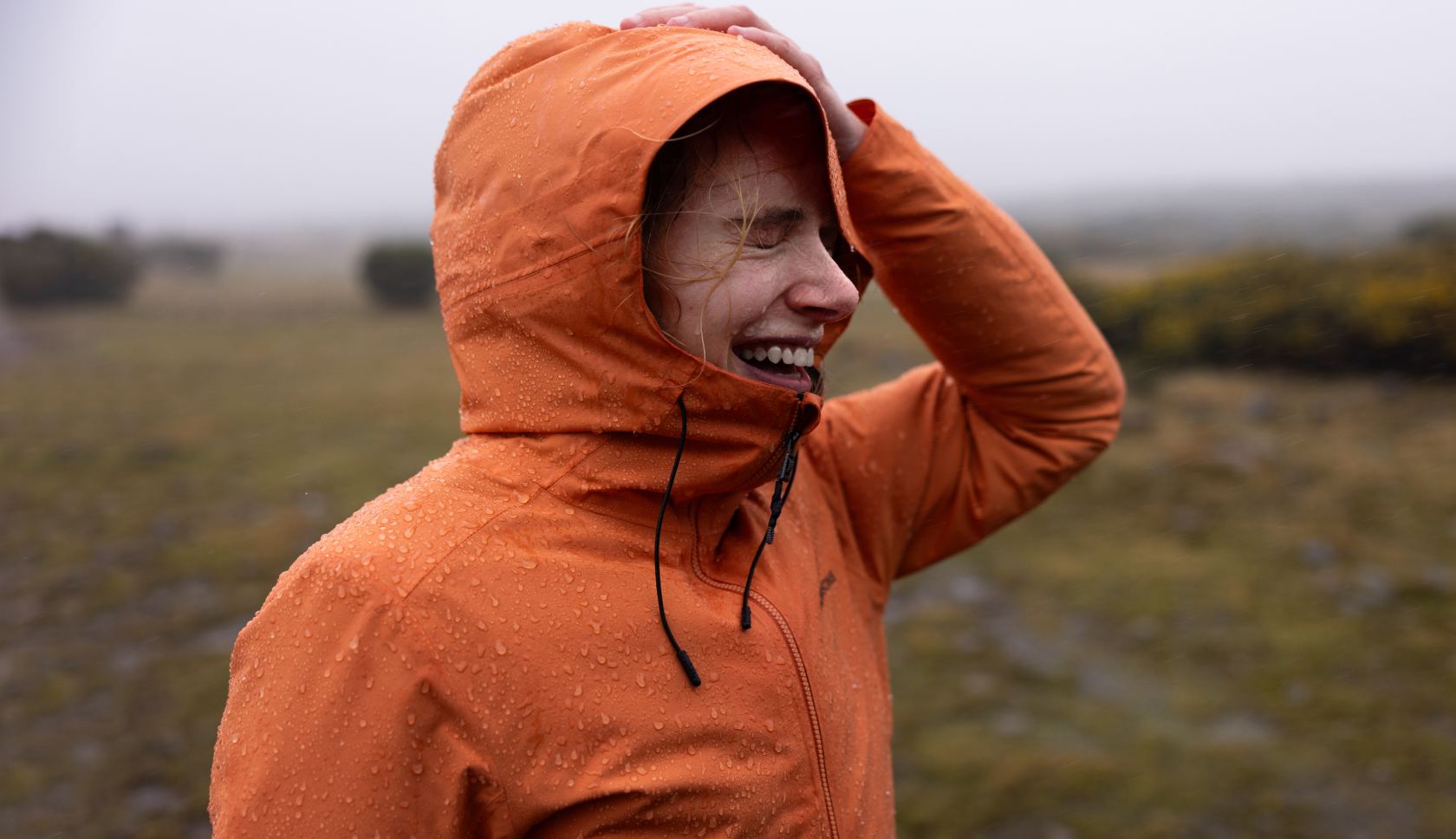 Vrouw met capuchon lacht in de natuur