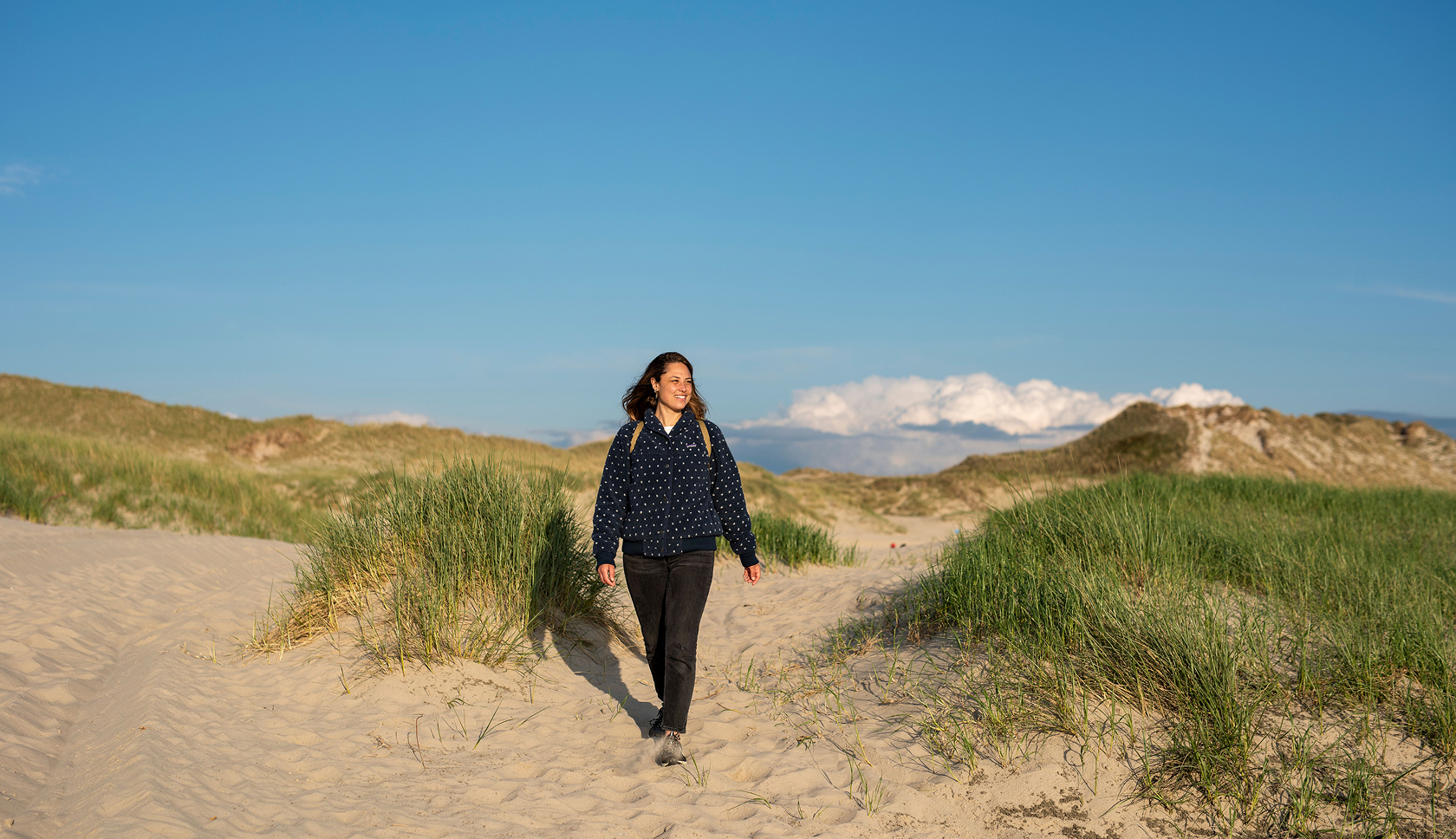 Een jonge vrouw loopt een NS-route door de duinen in gouden zonlicht