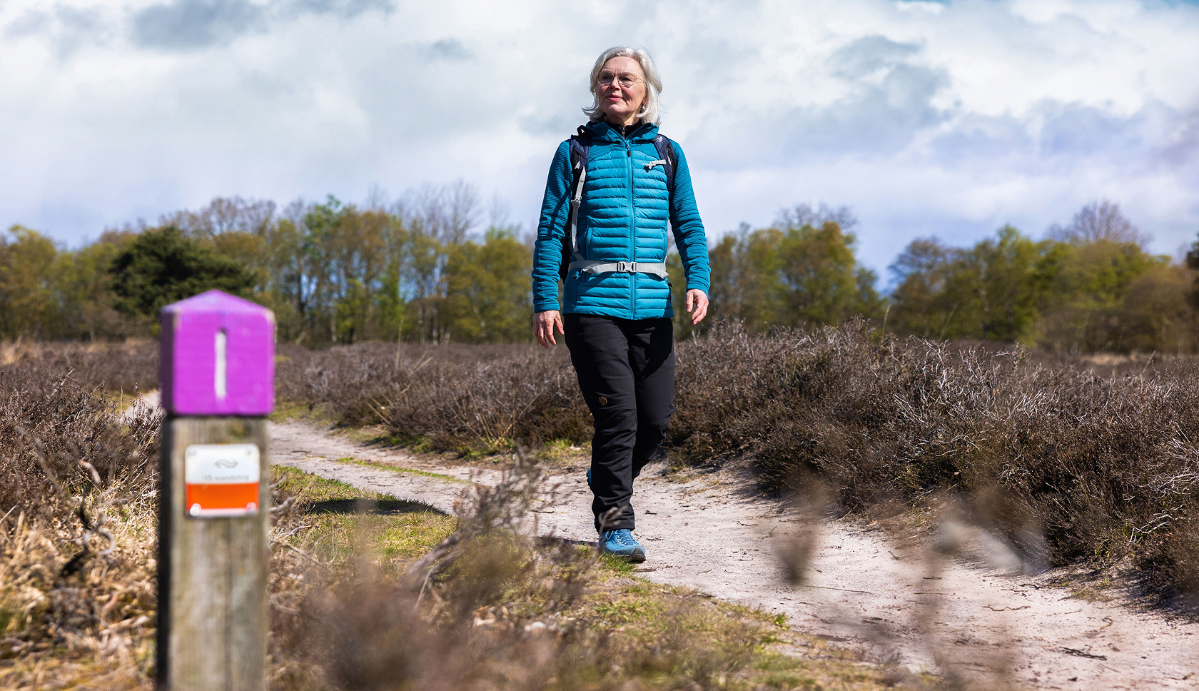 Een vrouw loopt een NS-wandeling door heidegebied 