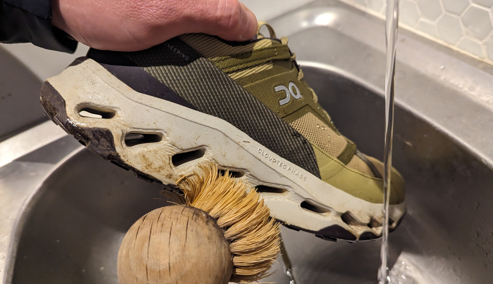 Een lage wandelschoen wordt met een borstel gepoetst onder een lopende waterkraan