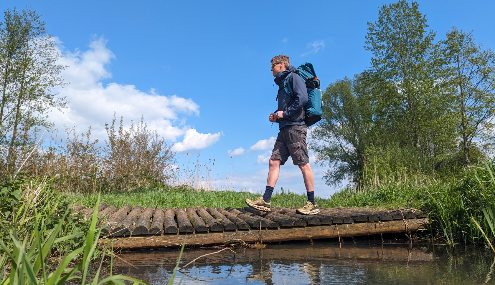 Een man met een rugzak loopt over een bruggetje over het water