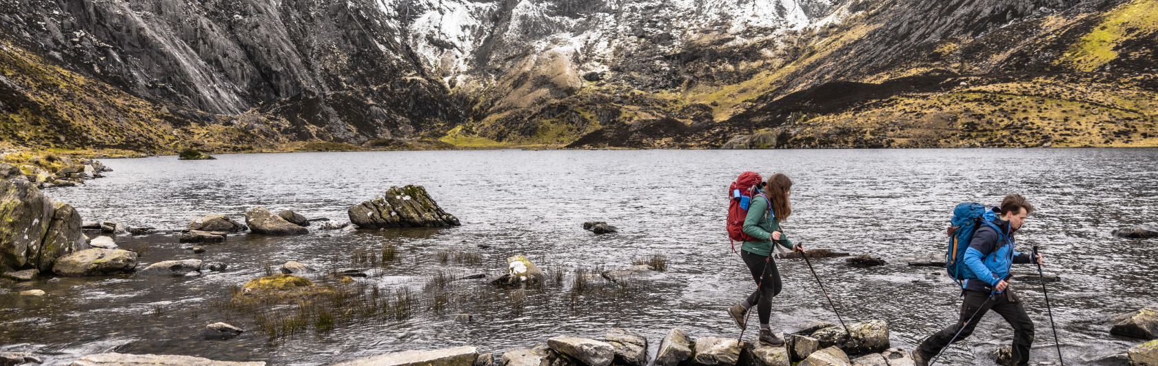 Twee mensen wandelen over stenen door een rivier