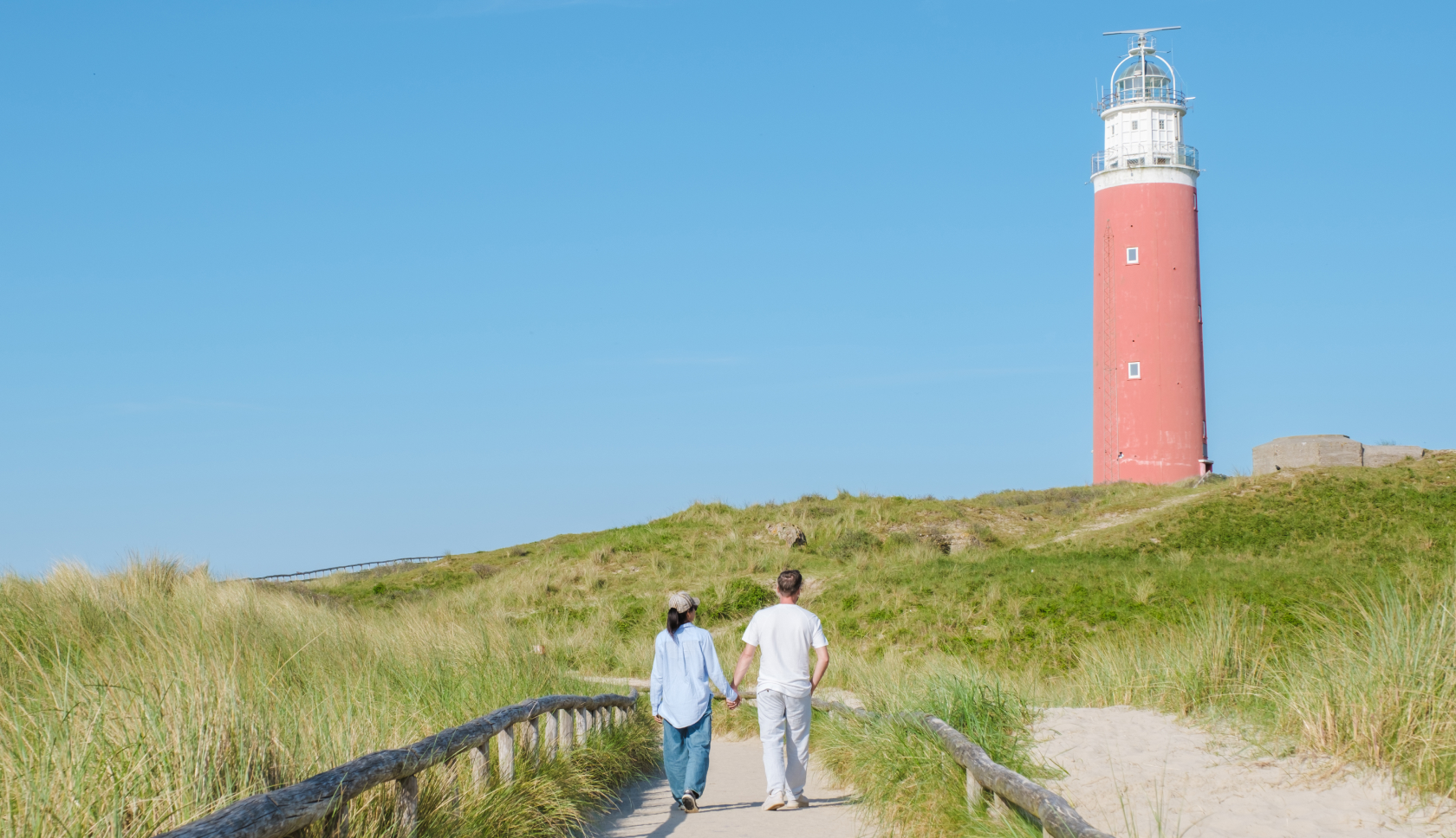 twee jongeren wandelen hand in hand over duinpad langs vuurtoren
