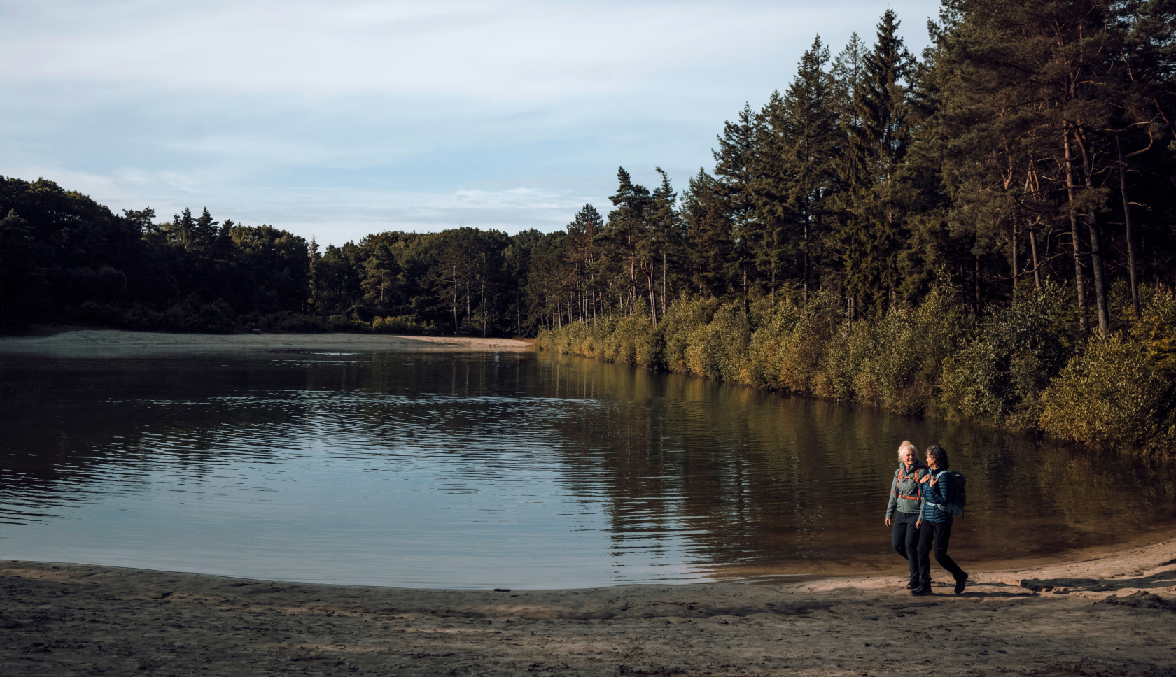 Twee vrouwen wandelen door mul zand langs een meertje