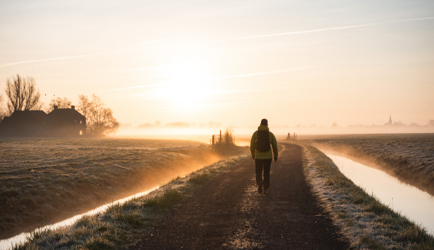 Een man loopt door een mistig polderlandschap van het Ziltepad bij gouden ochtendlicht