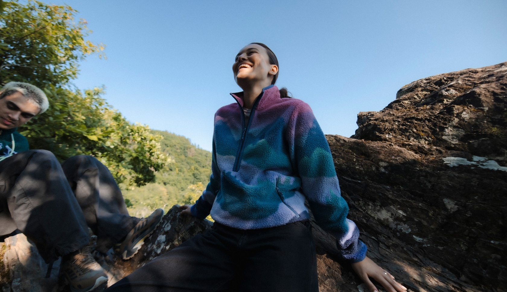Vrouw in een kleurrijke fleecetrui geniet van de buitenlucht in een bos.