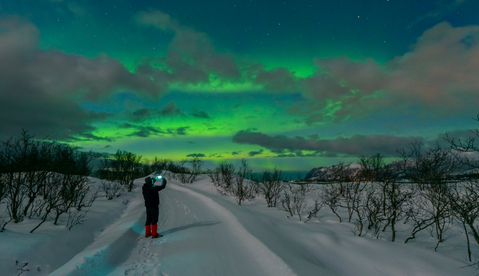 Iemand maakt met een smartphone een foto van het noorderlicht en een besneeuwd landschap.