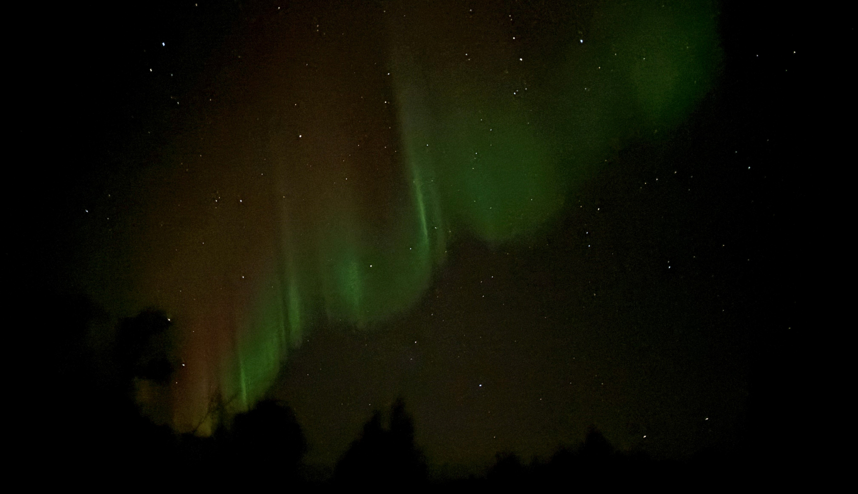 Een zwak noorderlicht tekent zich af tegen de sterrenhemel.