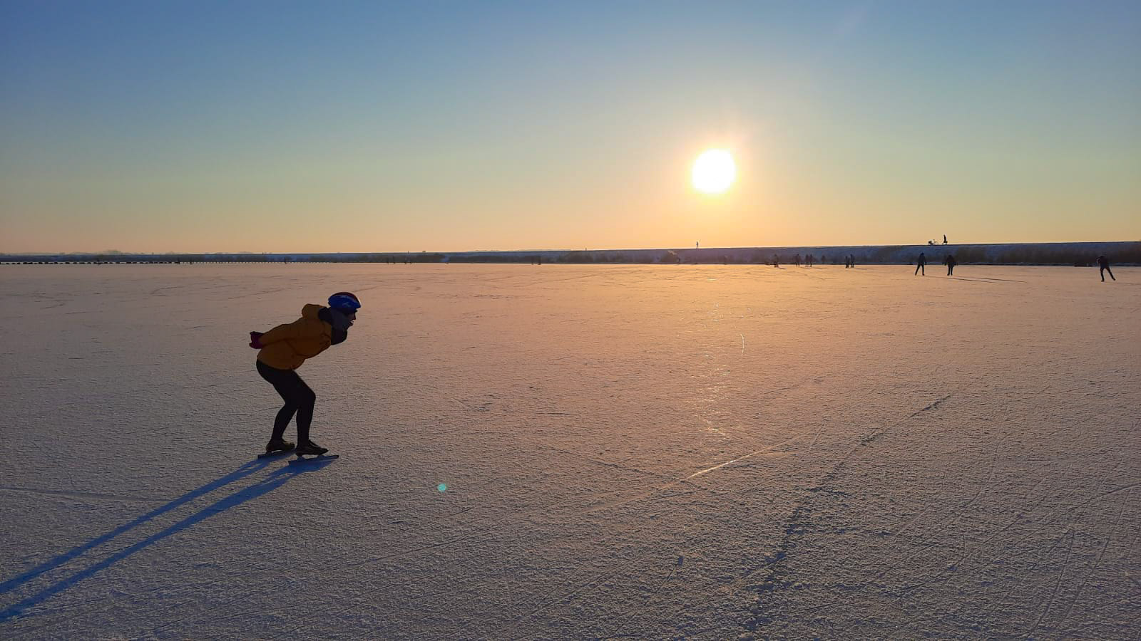 schaatsers op natuurijs met laaghangende zon