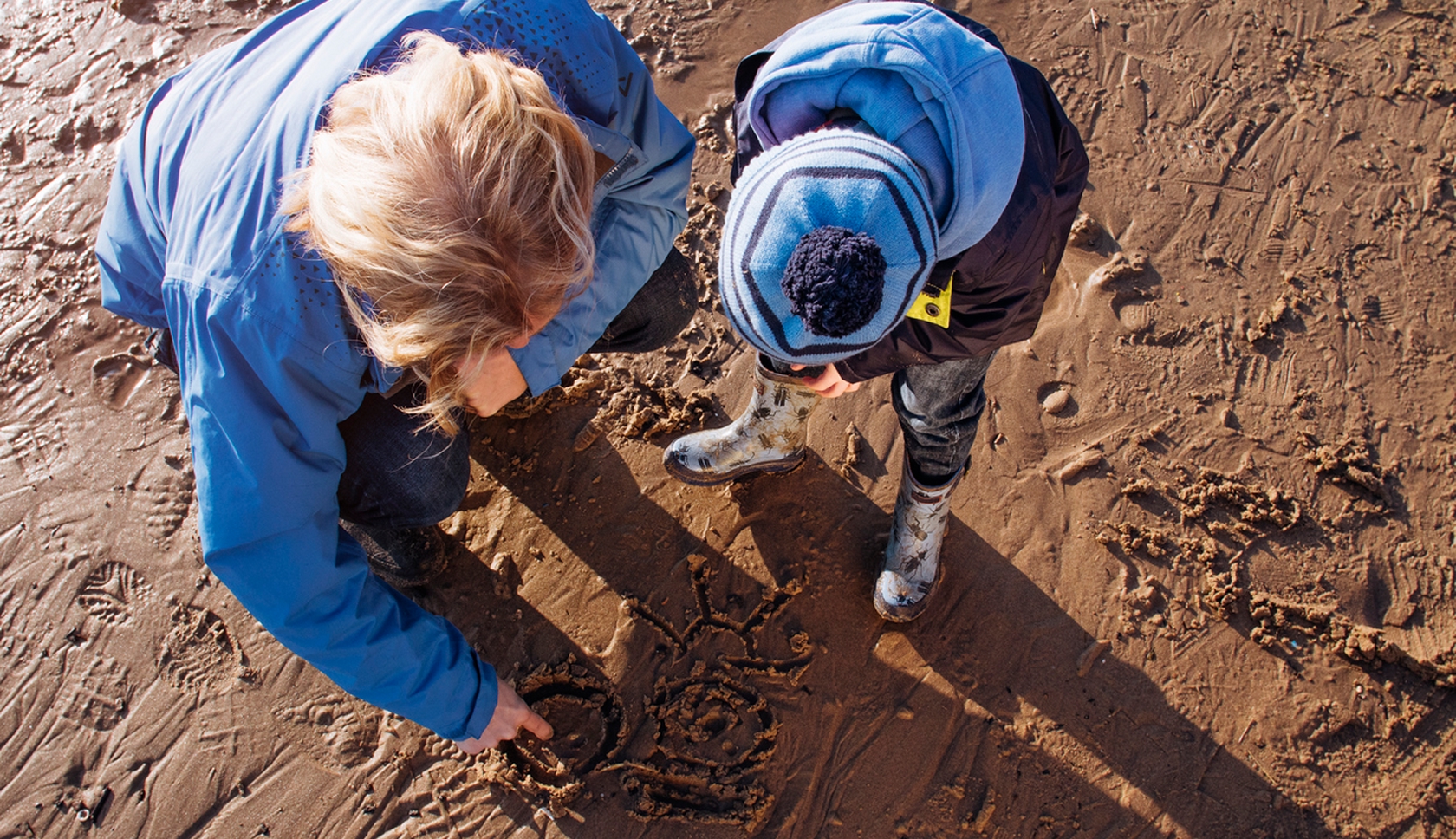 Volwassene en kind tekenen samen in het natte zand op het strand