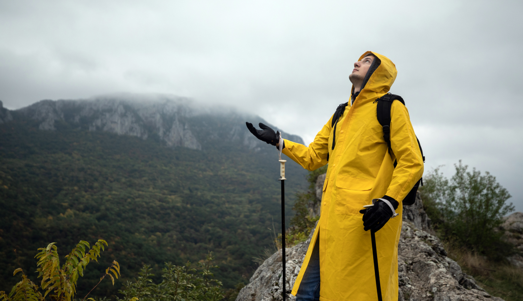man met gele regenjas en waterdichte handschoenen voelt voor regen in de bergen