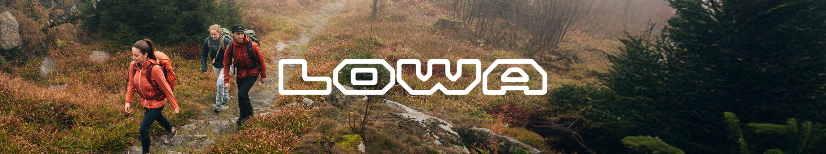 Drie wandelaars met LOWA-wandelschoenen en rugzakken lopen door een heuvelachtig boslandschap, met het LOWA-logo centraal in beeld.