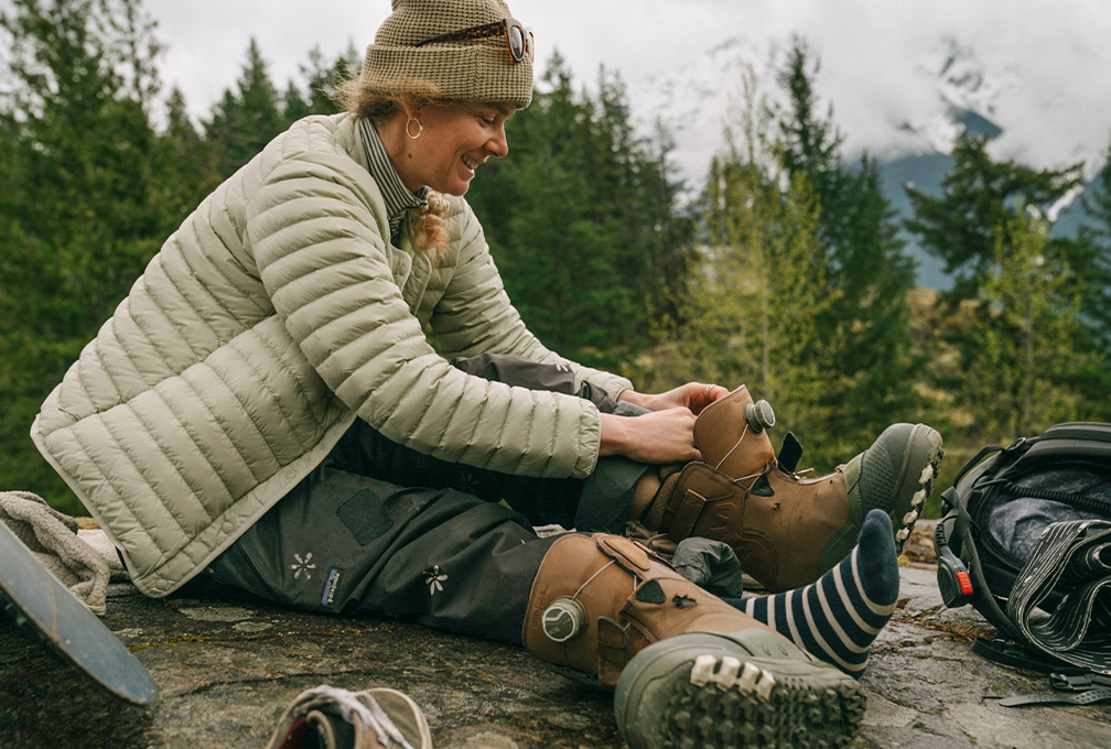 Wandelaar in Patagonia-outdoorkleding trekt wandelschoenen aan in een bergachtig natuurgebied.