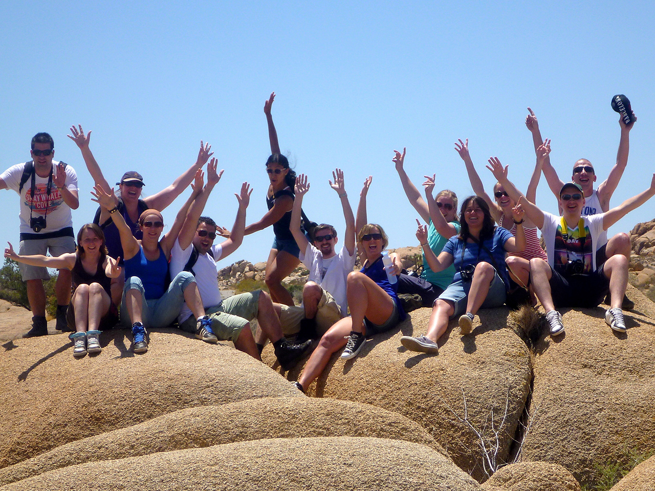 Sawadee - group of travelers sitting on boulders, waving at the camera