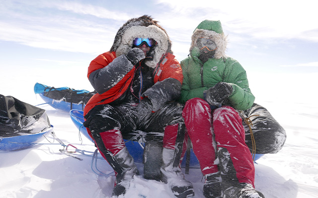 twee personen in dikke bepakking zitten op slee in de sneeuw