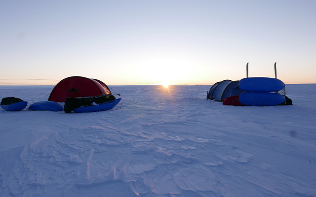twee tenten in de sneeuw met de ondergaande zon in de achtergrond